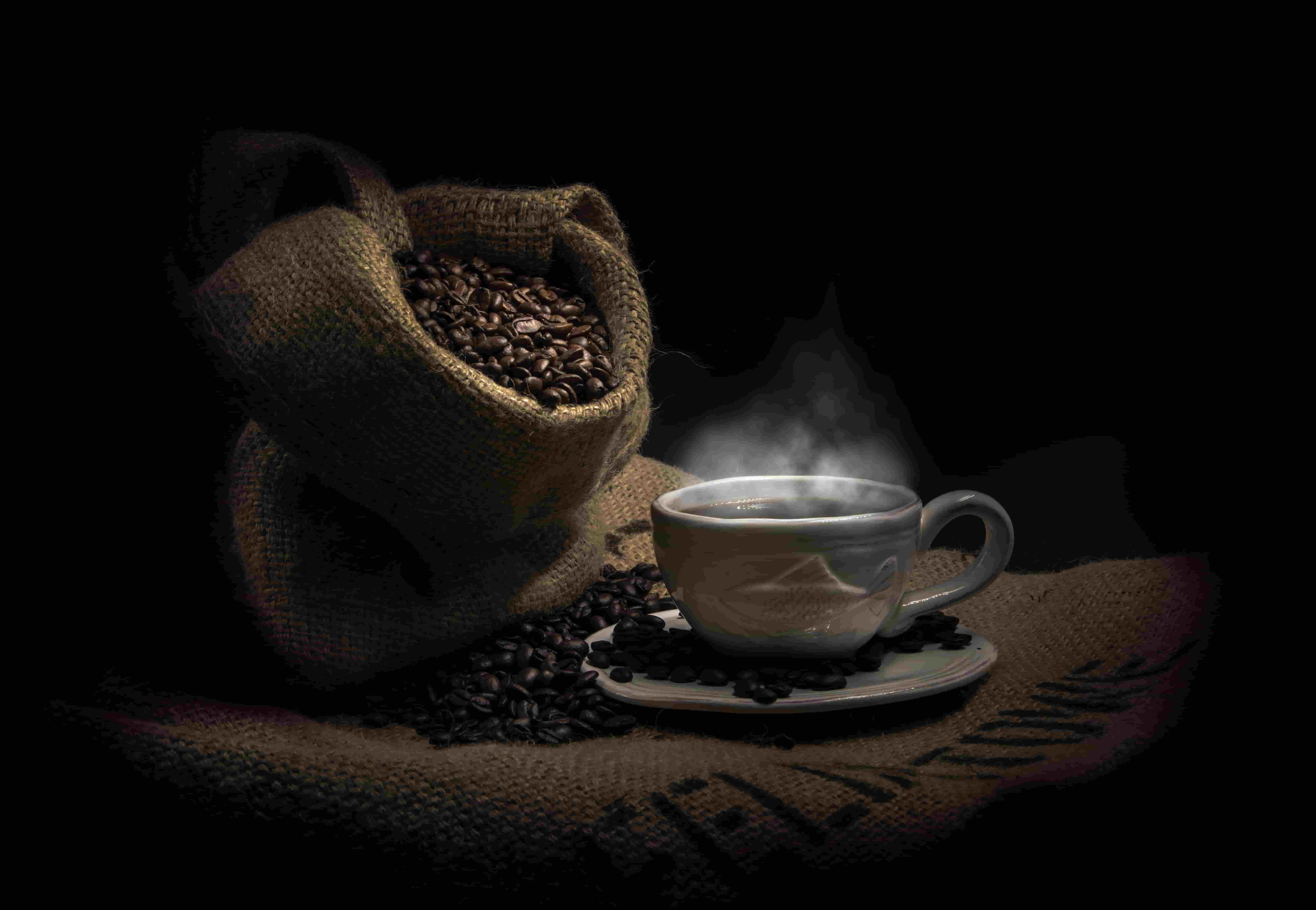 A hot cup of coffee with a bag of coffee beans at the side.